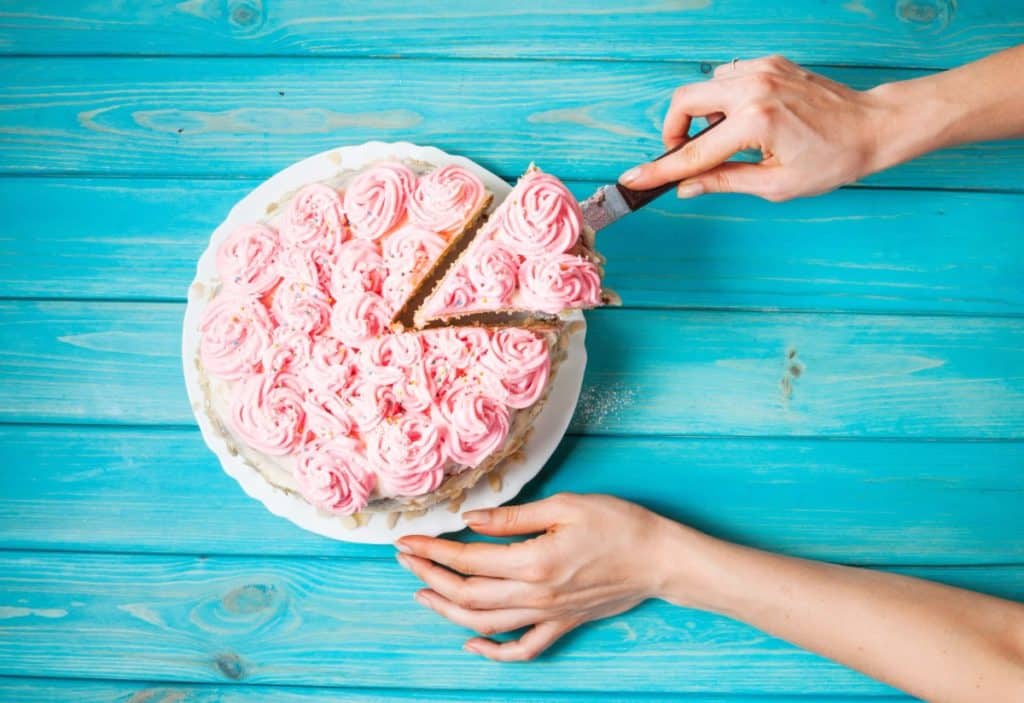 A cake slice is being removed from a round cake decorated with pink rosettes