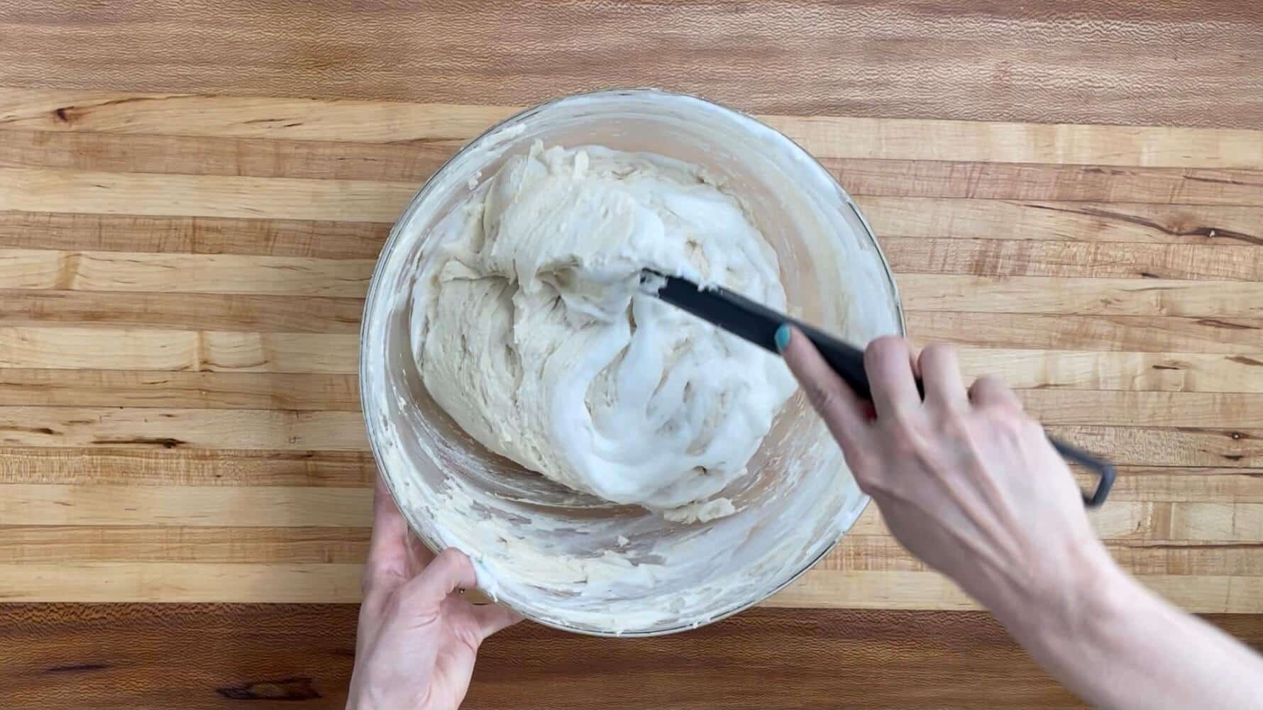 A bowl with vanilla cake batter with egg whites being folded in with a large spatula