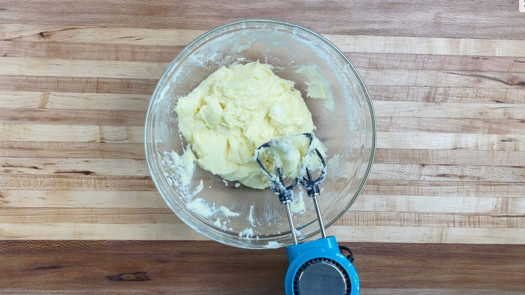 A bowl with creamed butter and other ingredients with a handheld mixer