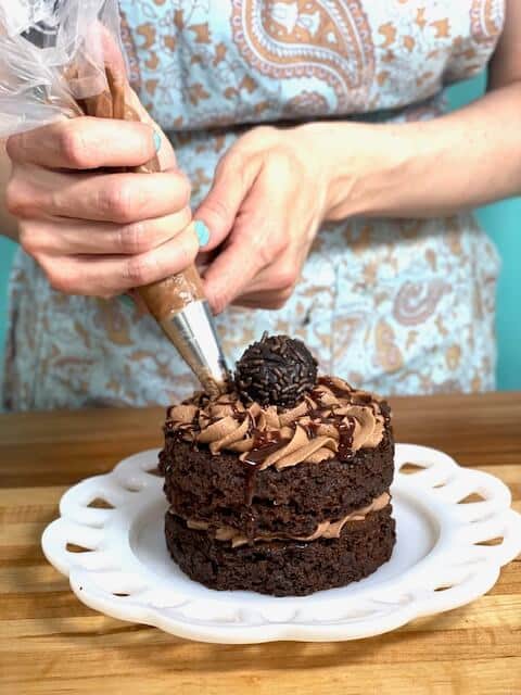 A mini moist chocolate cake being decorated with chocolate buttercream and a cake pop.