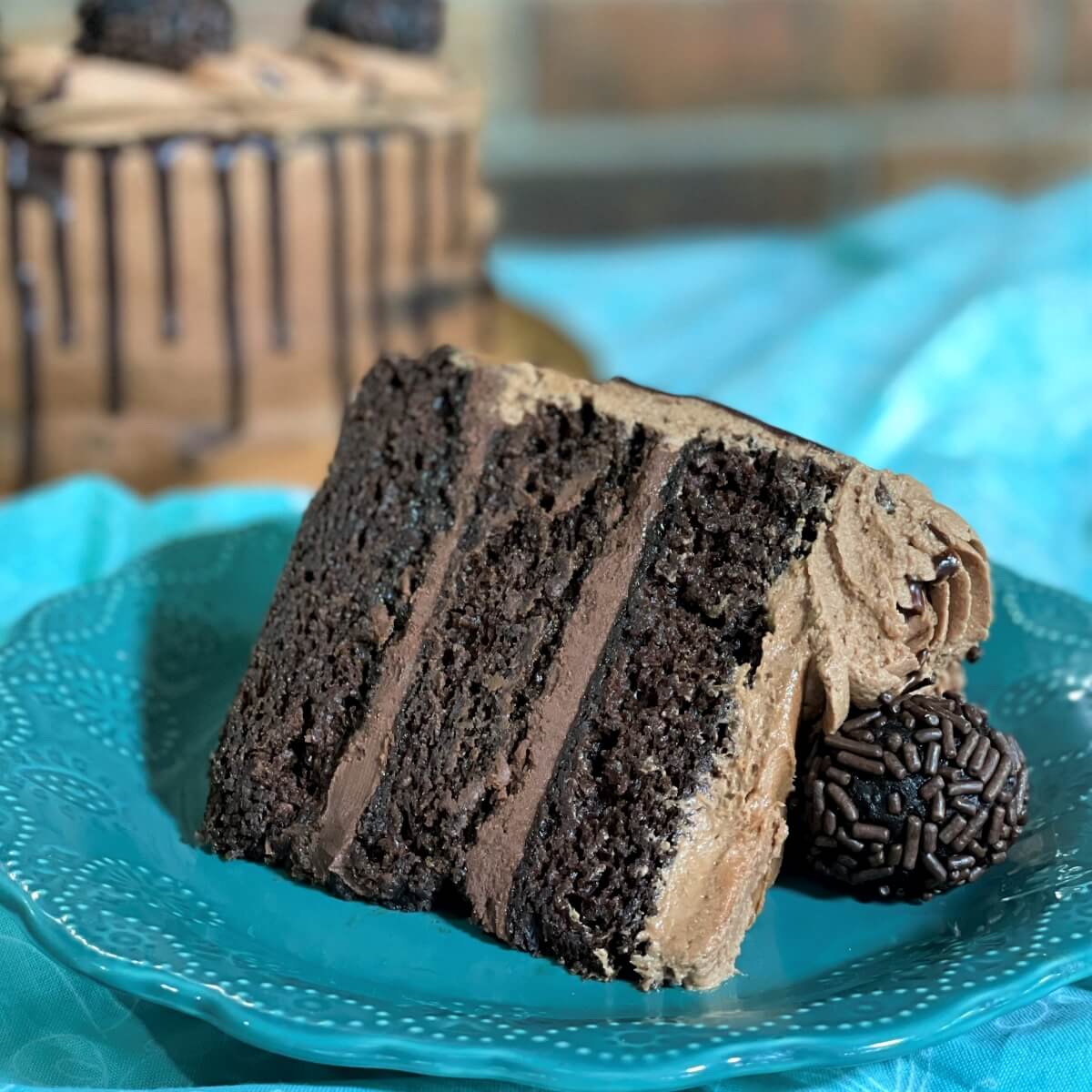 A slice of chocolate ganache layer cake on a teal plate.