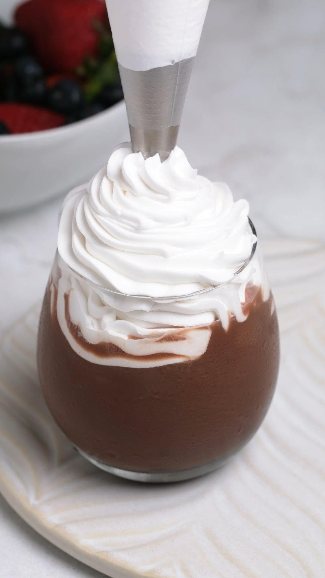 Thick stabilized whipped cream frosting being piped into a glass.