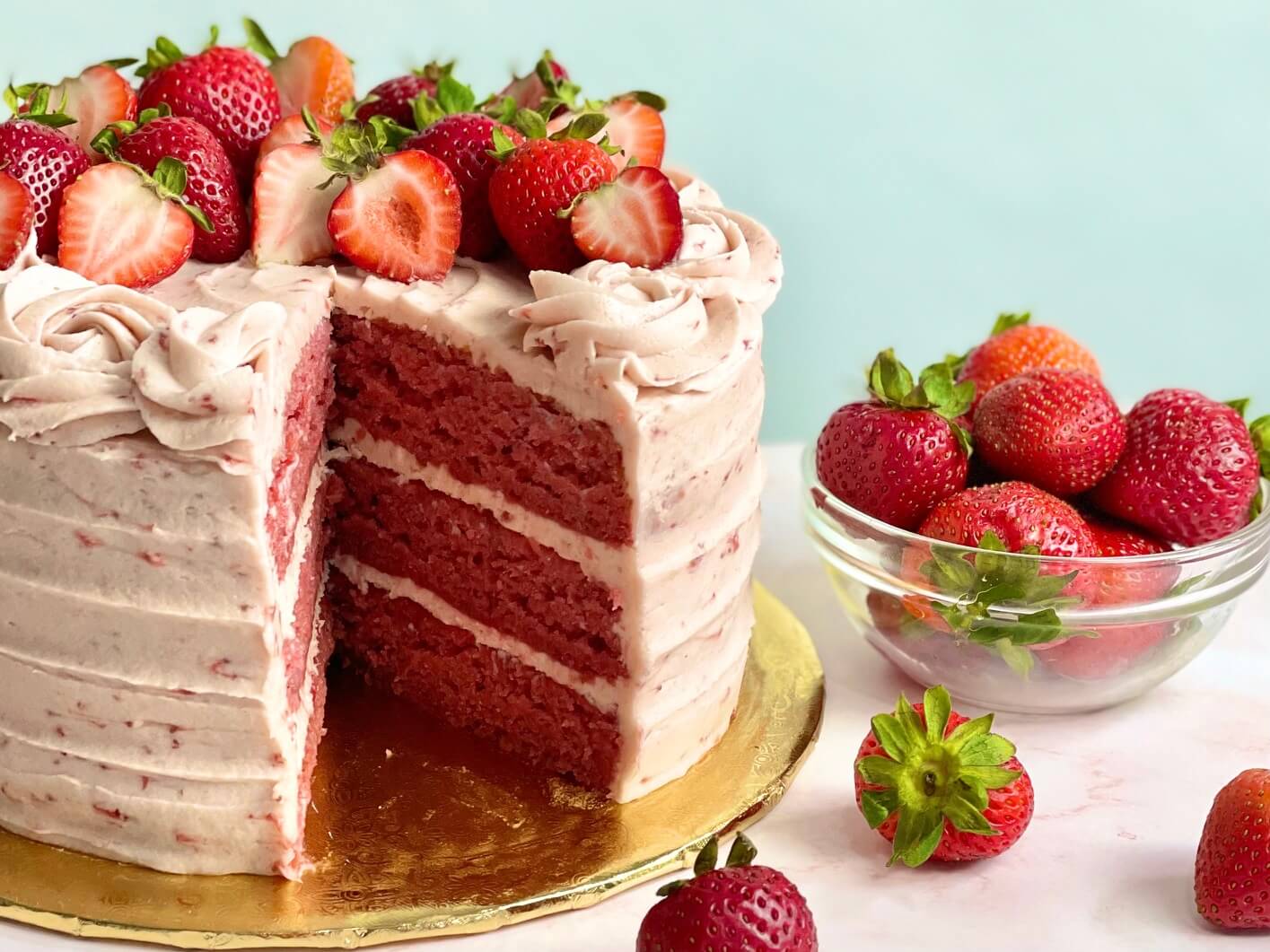 Homemade Strawberry Cake cut open showing three layers and a bowl of fresh strawberries.