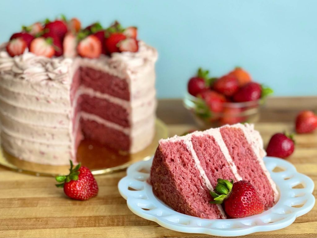 Fresh Strawberry Cake cut open showing the cake layers and a slice on a plate.