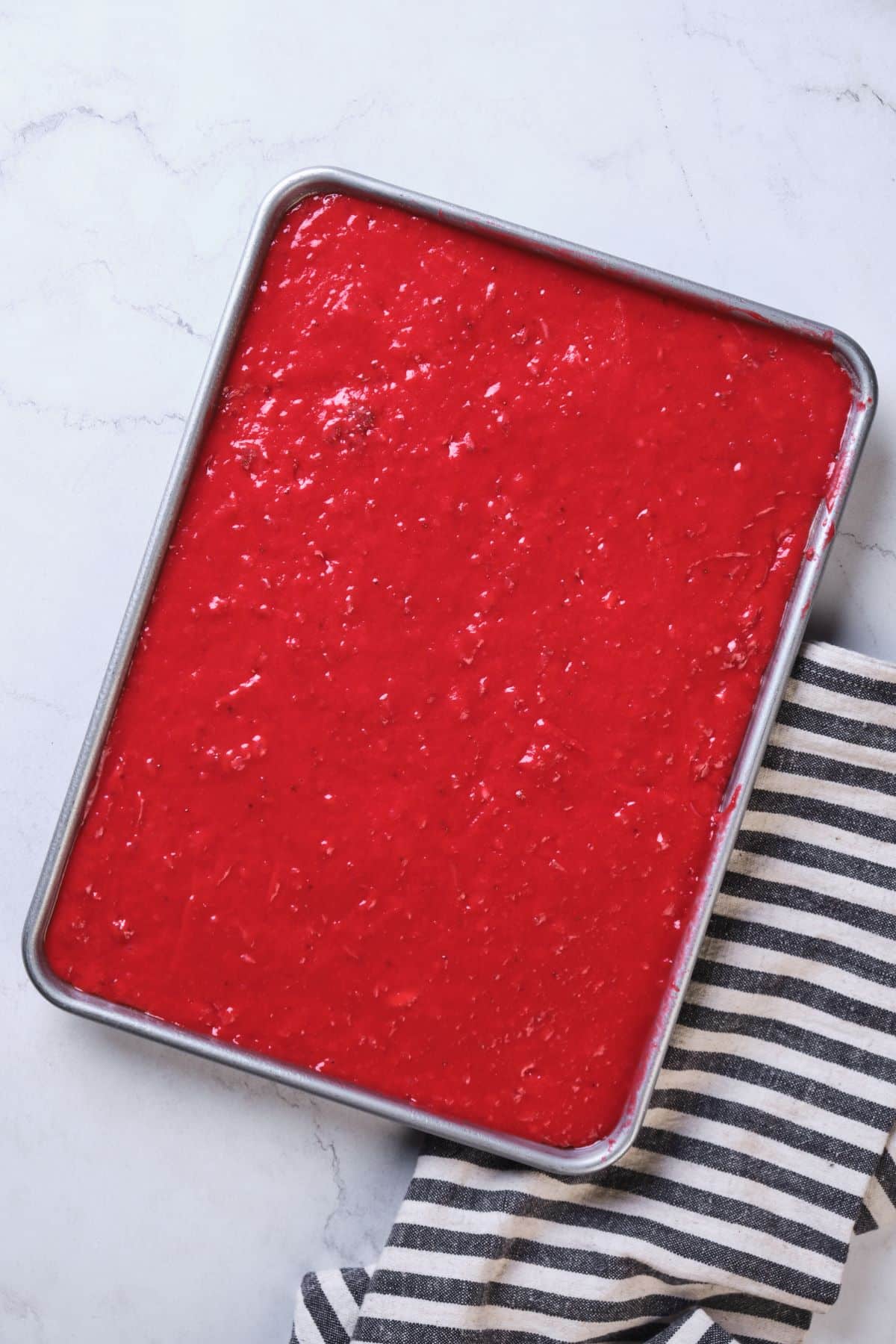 The fresh strawberry cake batter spread out in a cake pan.