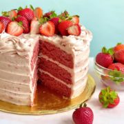 A 3-layer fresh strawberry cake with a large slice taken out so you can see the layers, plus a bowl of fresh strawberries