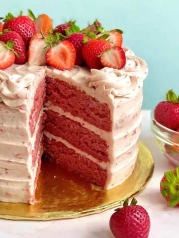 A 3-layer fresh strawberry cake with a large slice taken out so you can see the layers, plus a bowl of fresh strawberries