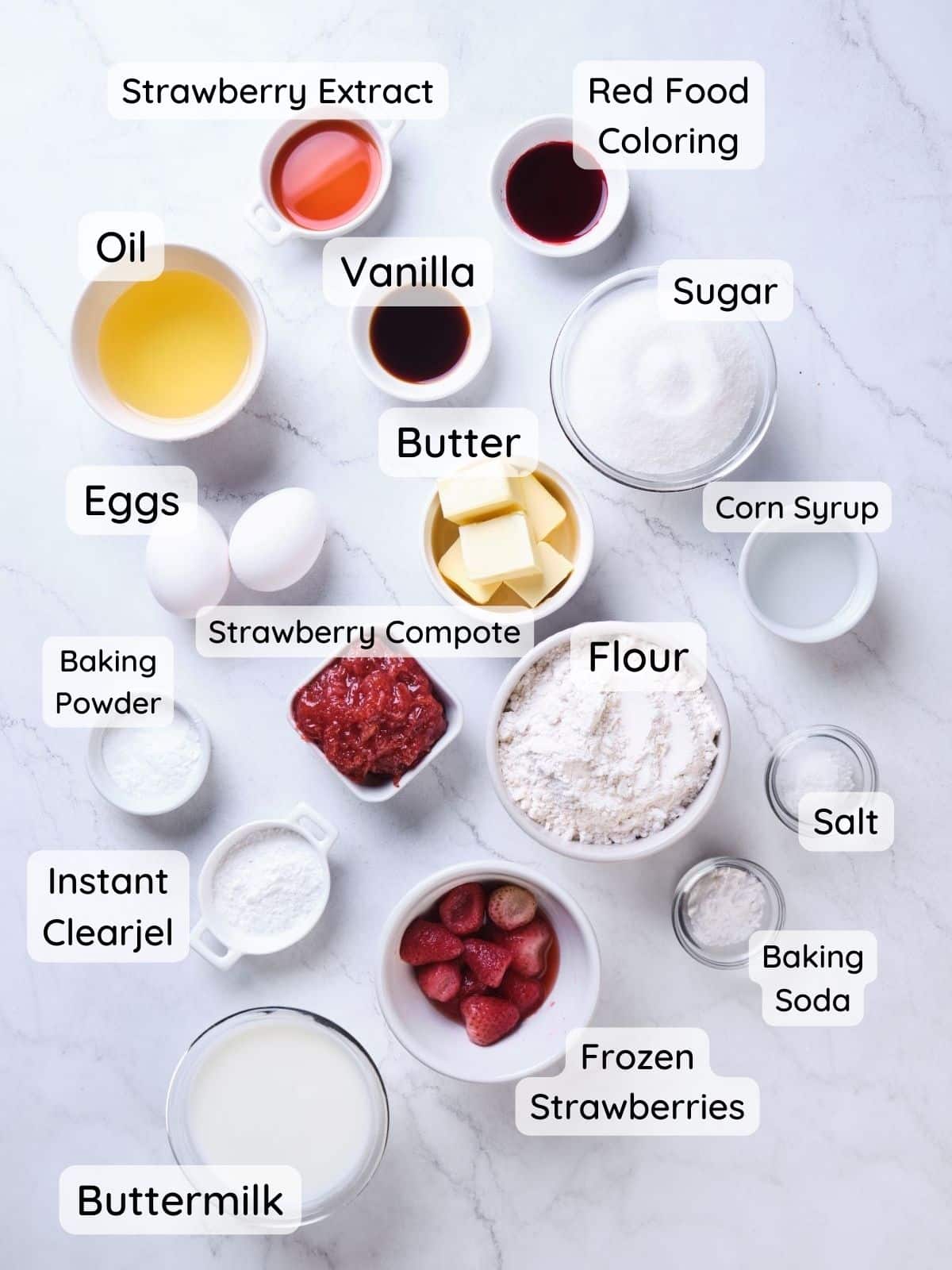 An overhead shot of the strawberry cake ingredients, with the text "flour, sugar, baking powder, baking soda, salt, instant clearjel, frozen strawberries, strawberry compote, eggs, buttermilk, oil, strawberry extract, vanilla, corn syrup, butter, red food coloring."