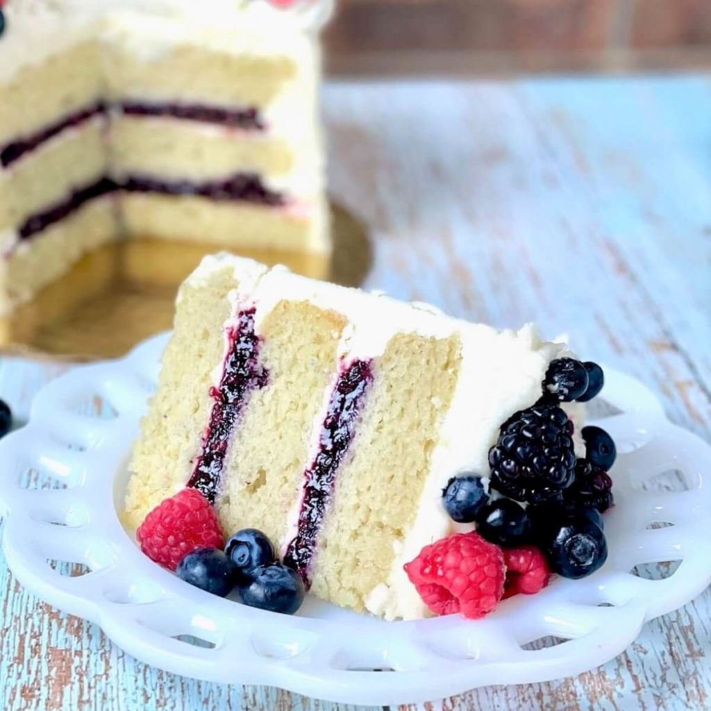 slice of vanilla cake made with the reverse creaming method with berry filling and a bowl of mixed berry cake filling