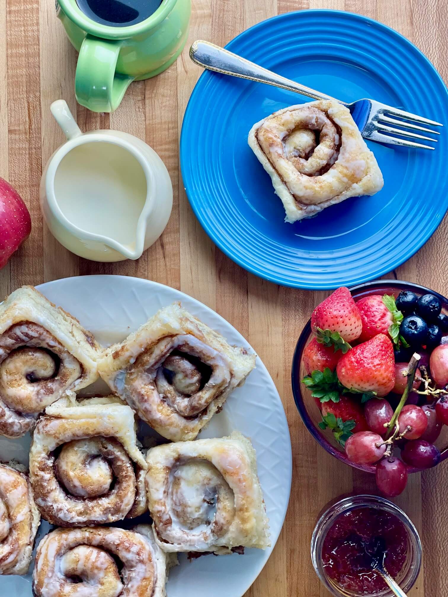 A plate of Mini Cinnamon Rolls on a table with fruit, coffee, and cream.