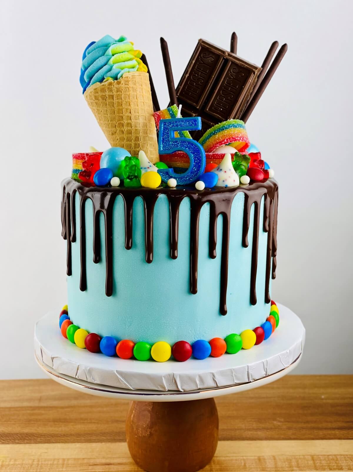 a blue cake with a chocolate ganache drizzle on a cake stand