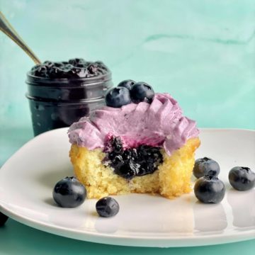a vanilla cupcake with blueberry cupcake filling and a bowl of blueberry compote filling in the background