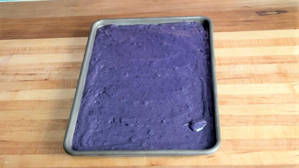 A sheet pan with blueberry cake batter inside.