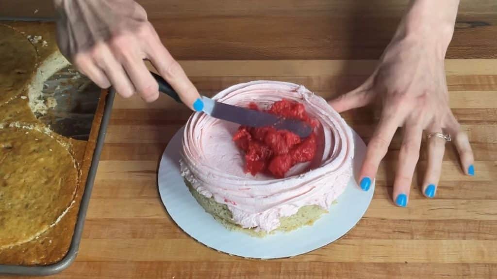 a layer of banana cake being filled with strawberry buttercream and strawberry compote filling