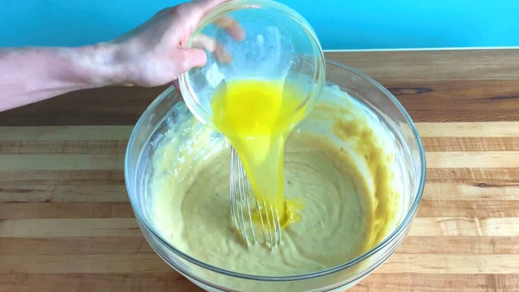 melted butter being poured over a bowl of banana cake batter for the banana cake recipe
