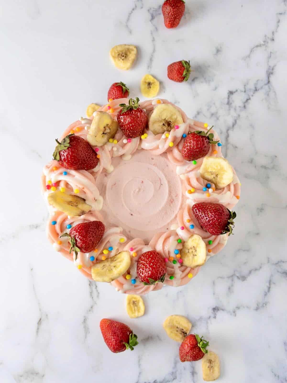 an overhead shot of strawberry banana cake topped with fresh strawberries and banana chips