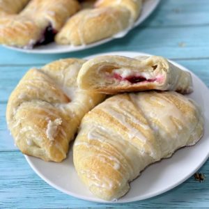 A closeup of soft cream cheese danish pastries, one open with the cream cheese and cherry filling showing on the inside.