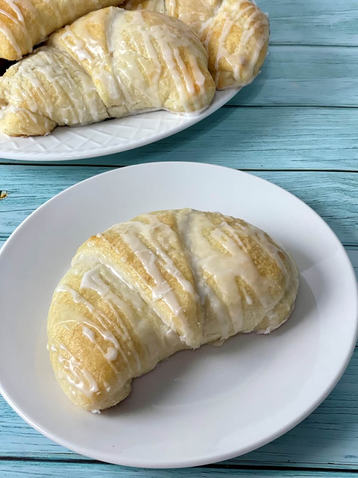 A plate with a large fluffy cream cheese danish on it, with more soft danishes pictured in the background.