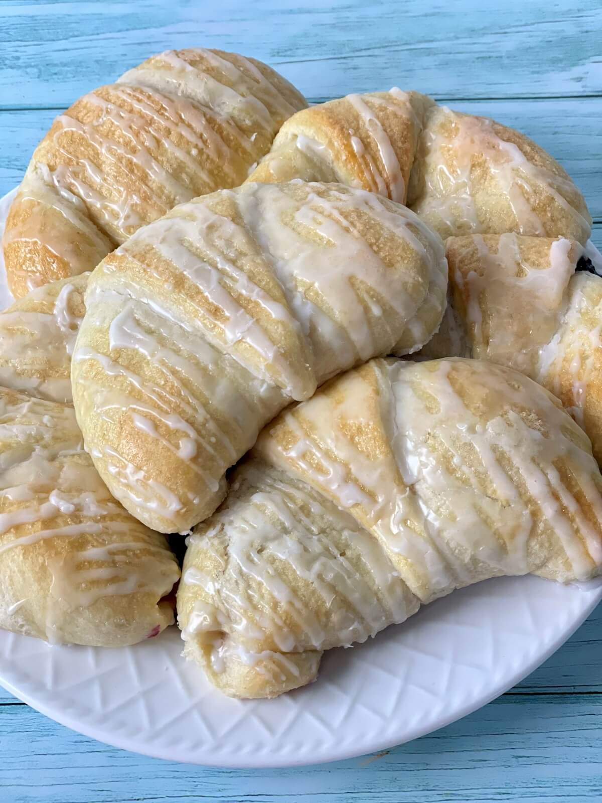 A closeup of a plate of large soft and fluffy cheese danish with glaze.