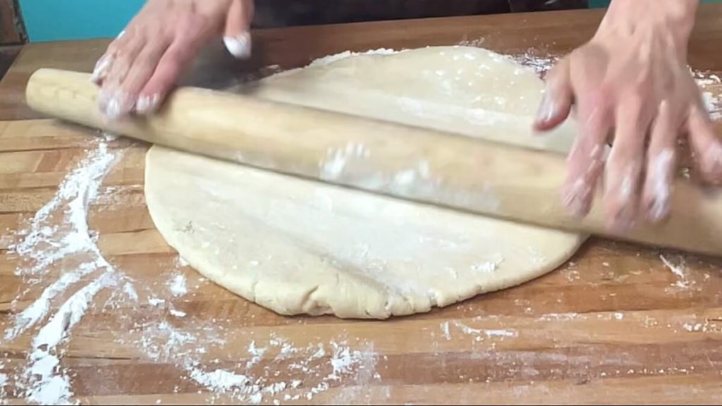 A circle of danish dough being rolled out with a rolling pin.