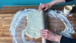 Danish dough being rolled out with a rolling pin on a floured surface.