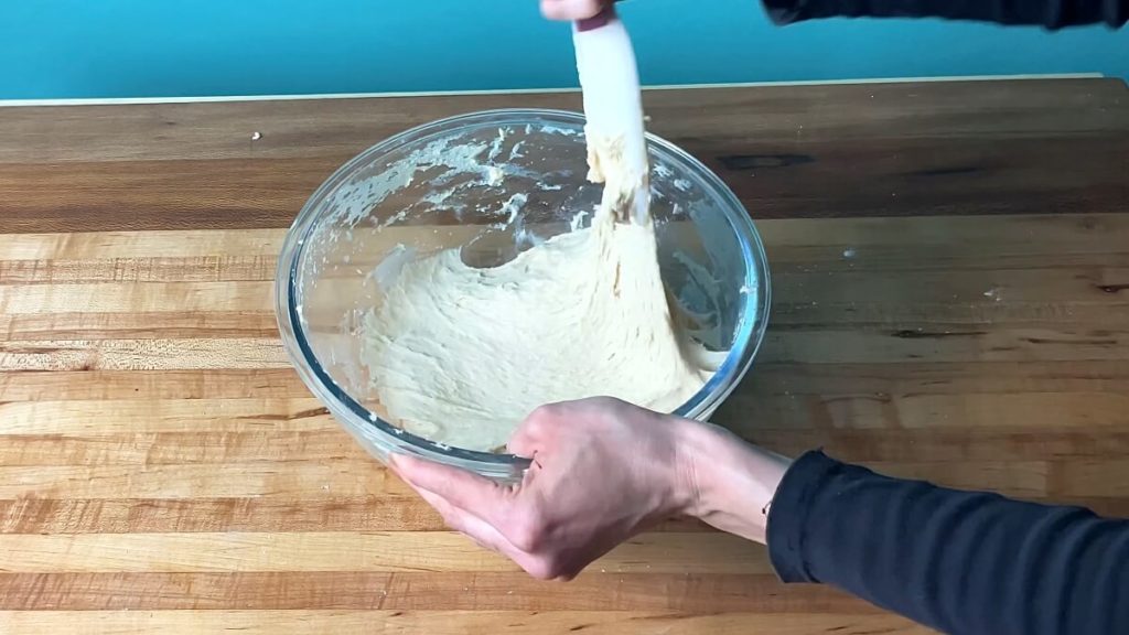 A bowl of sticky but smooth dough being stirred with a spatula.