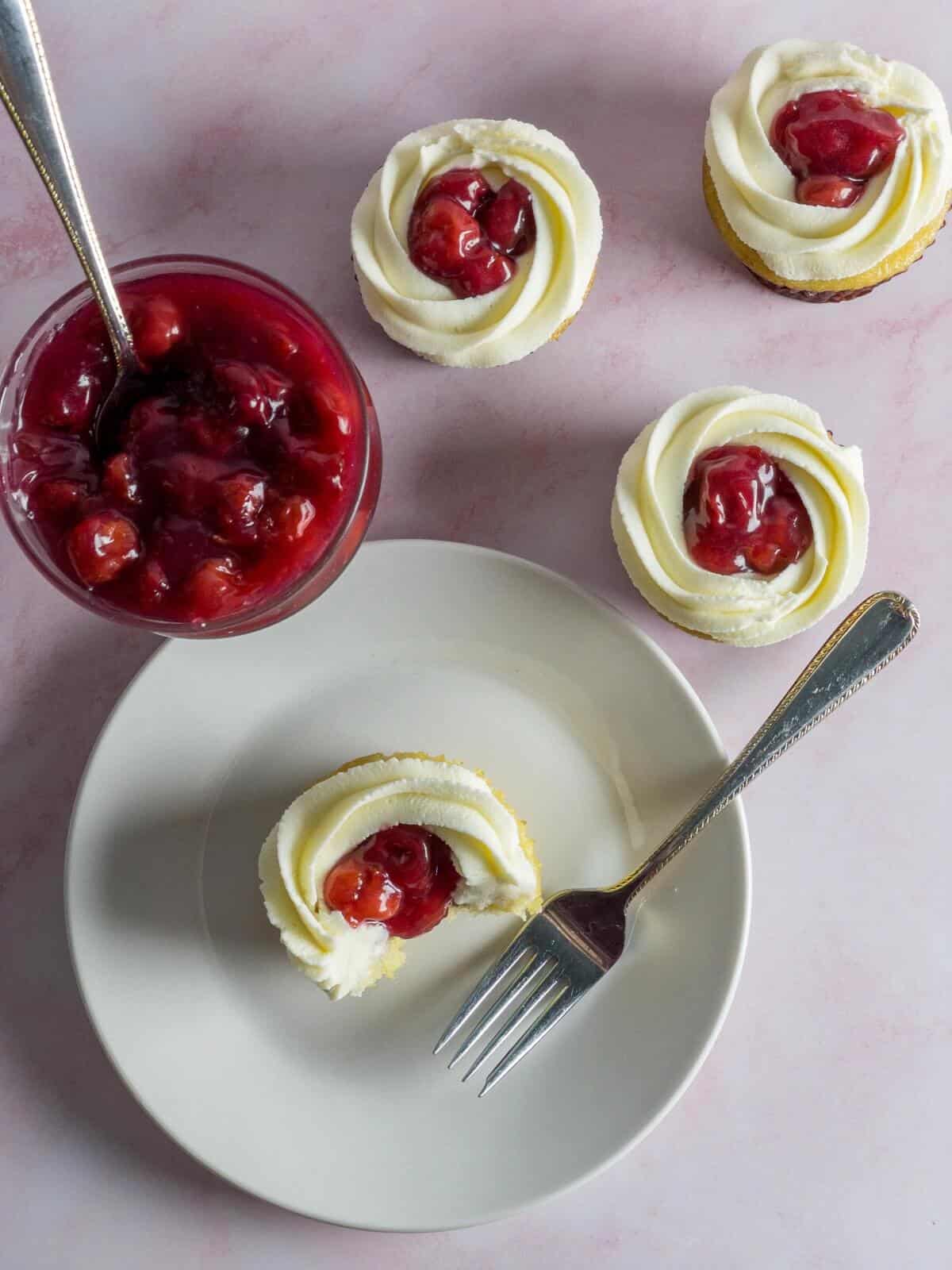An overhead shot of a bowl with bright red tart cherry filling and cupcakes filled with it