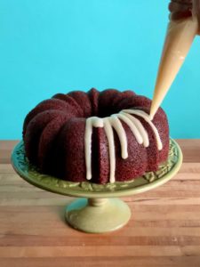 A red velvet bundt cake with icing being drizzled on top with a piping bag