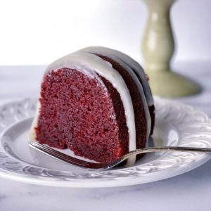 A slice of deep red moist red velvet bundt cake with cream cheese glaze