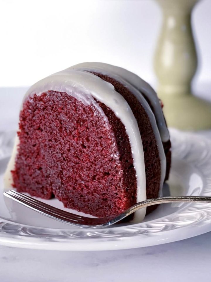 A slice of deep red moist red velvet bundt cake with cream cheese glaze