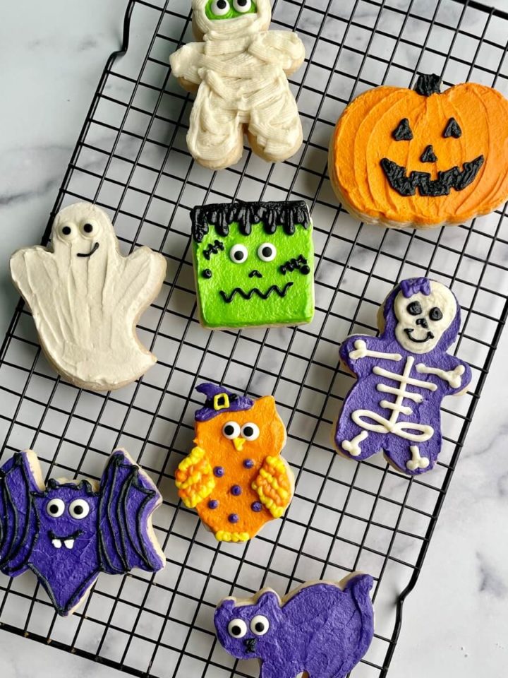Several Halloween buttercream decorated sugar cookies on a cooling rack