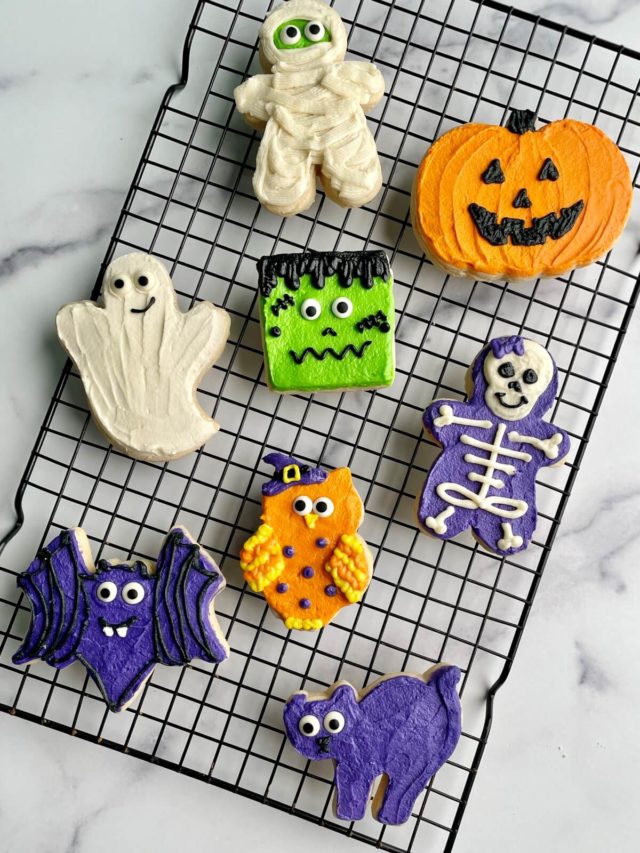 Several Halloween buttercream decorated sugar cookies on a cooling rack