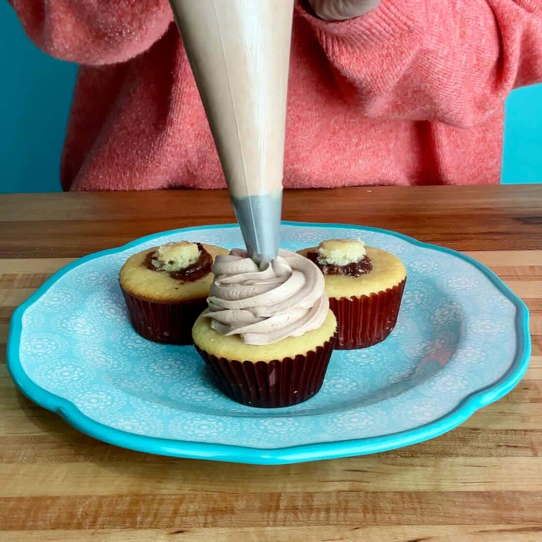 filled nutella cupcakes being frosted with nutella buttercream with a piping bag