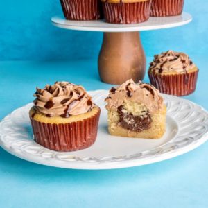 Nutella cupcakes on a plate with more in the background, and one cupcake is cut open showing the nutella filling.