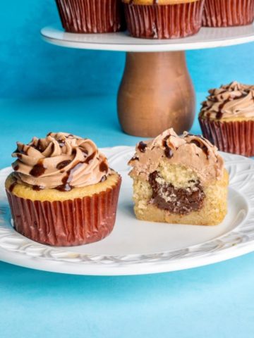 Nutella cupcakes on a plate with more in the background, and one cupcake is cut open showing the nutella filling.