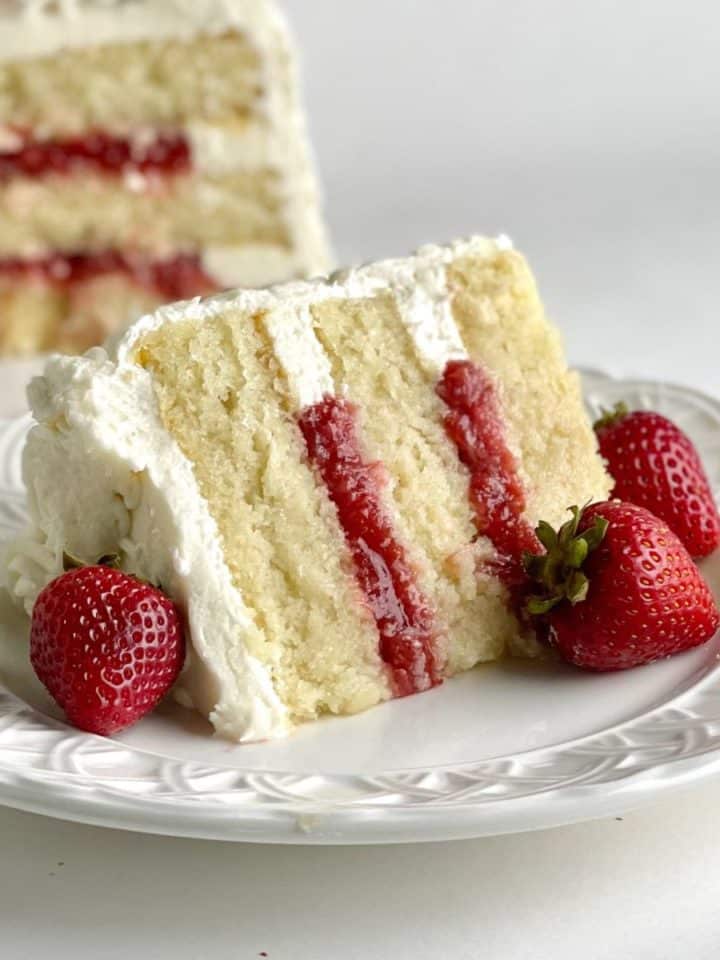 A Vanilla Cake Slice with Strawberry Cake Filling and the rest of the layered cake in the background.