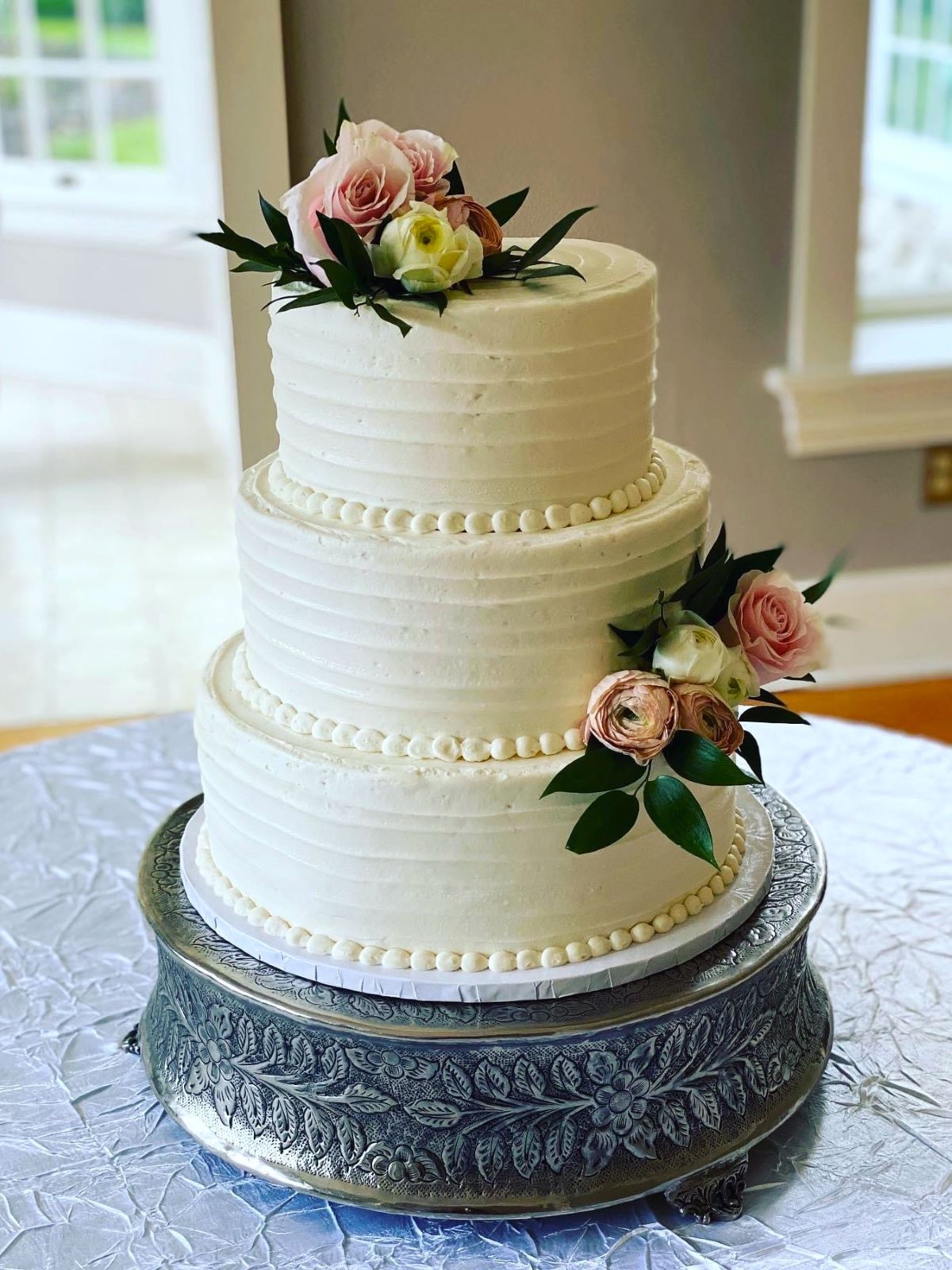 A three-tiered wedding cake that has been transported on a cake drum and then placed on a cake stand at the event venue.