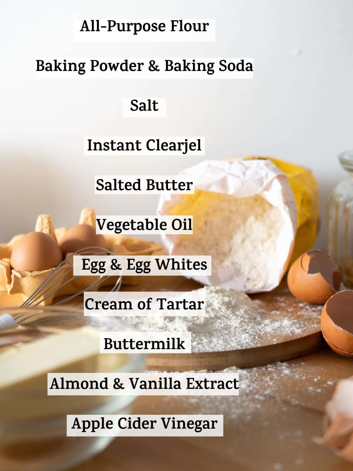 The ingredients for moist vanilla cake recipe listed over a photo of some baking ingredients. The text reads "all-purpose flour, baking powder and baking soda, salt, instant clearjel, sugar, salted butter, vegetable oil, light corn syrup, egg and egg whites, cream of tartar, buttermilk, almond and vanilla extract, apple cider vinegar.