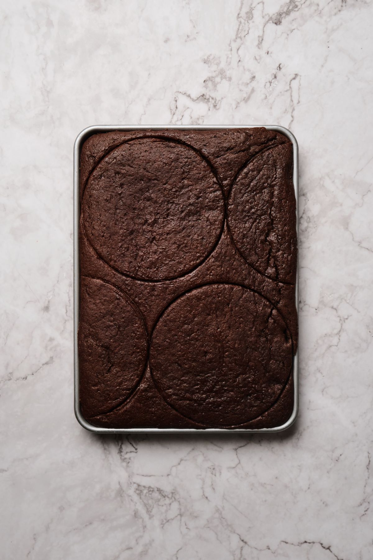 A ¼ sheet pan of chocolate cake with layers cut out using a cake ring.