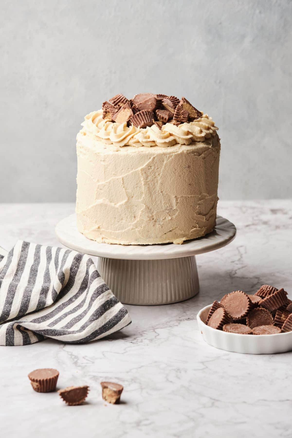 A Peanut Butter Chocolate Cake on a pedestal near some peanut butter cups,