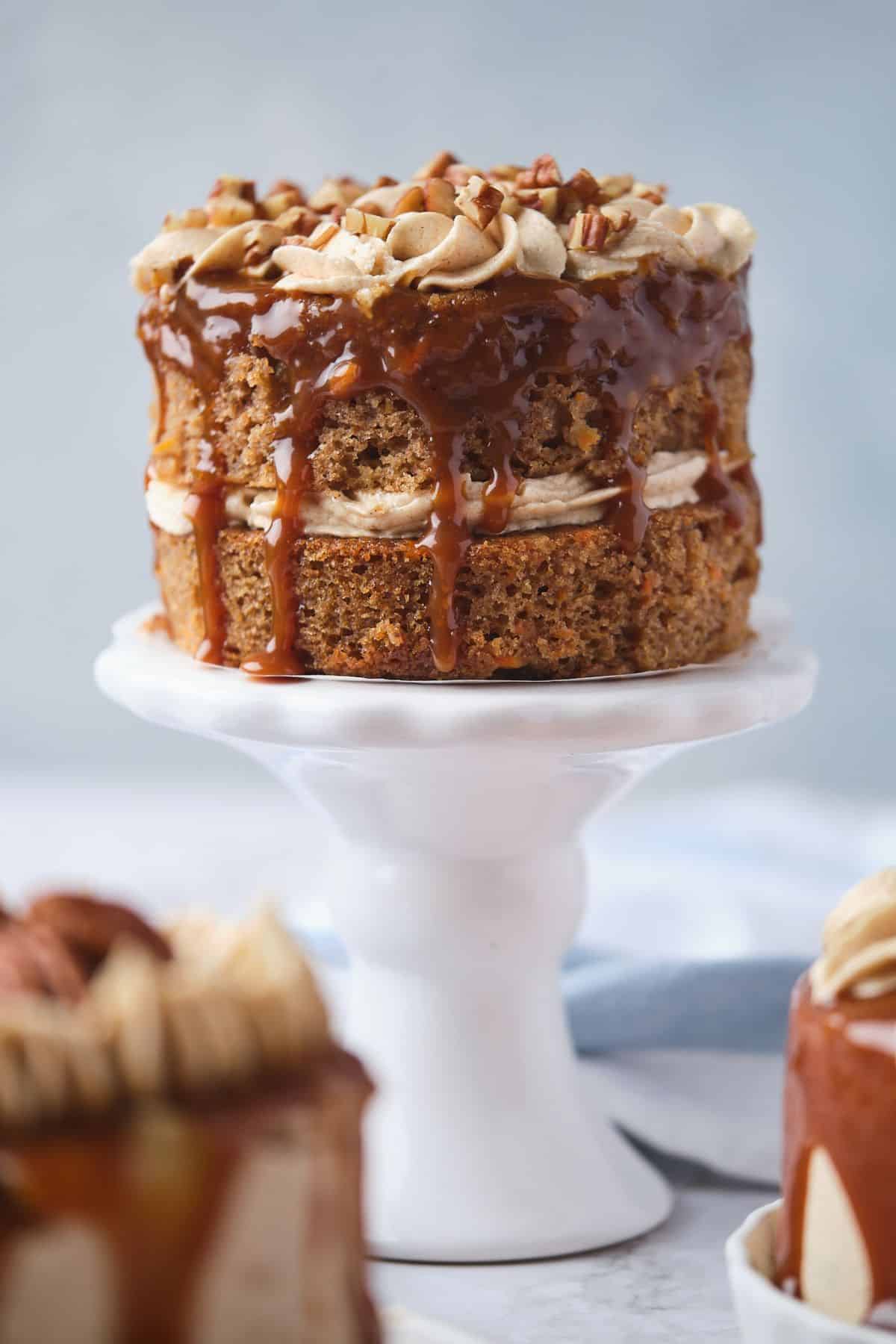 A closeup of a mini carrot cake with caramel drizzle, with two other mini carrot cakes nearby.