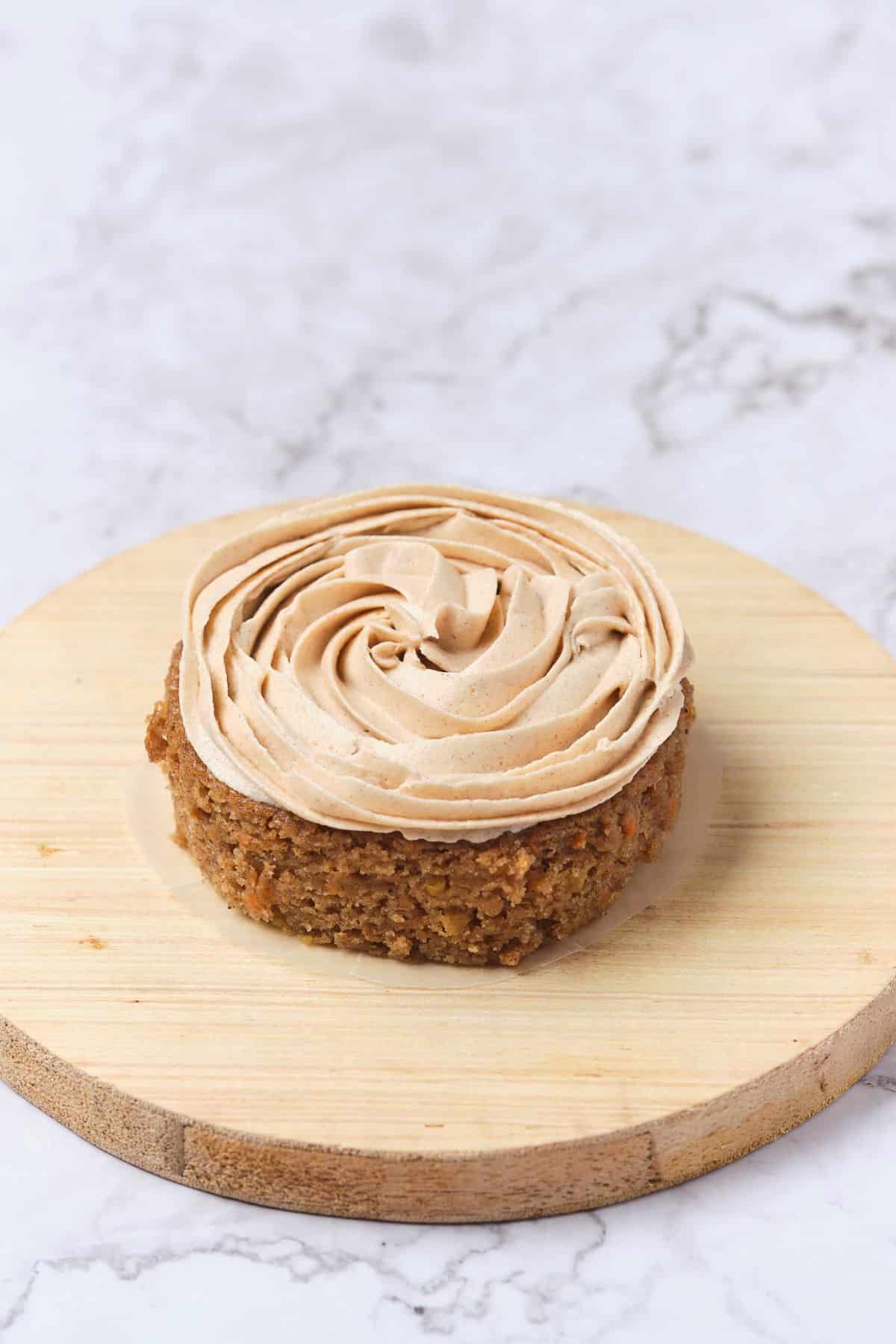 A small carrot cake being frosted with cinnamon cream cheese buttercream.