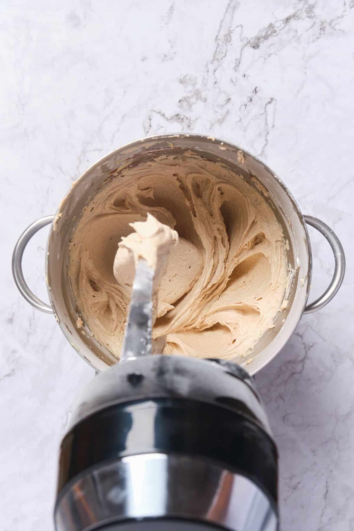 Cinnamon cream cheese buttercream frosting being prepared in a stand mixer.