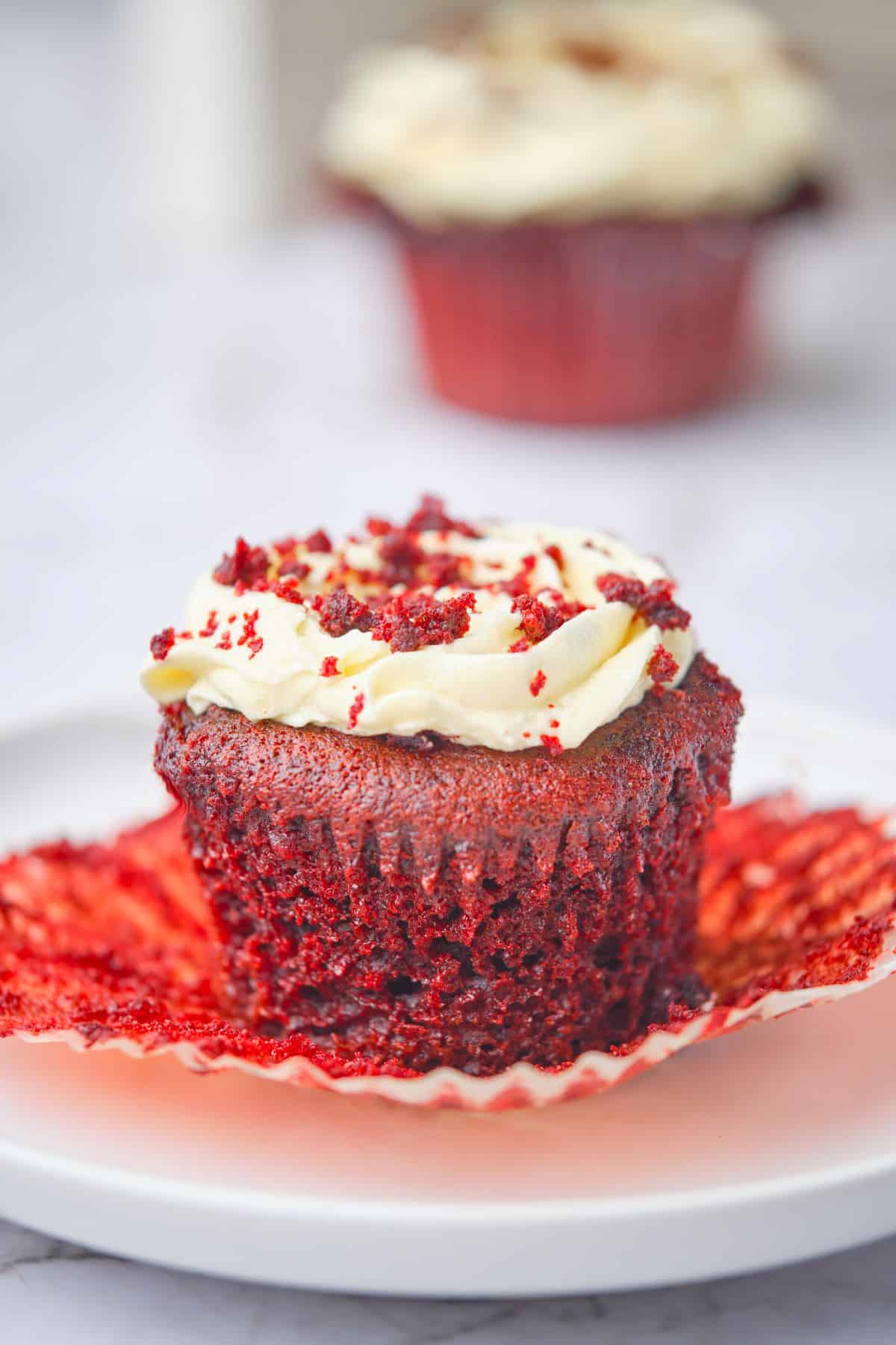 A super moist red velvet cupcake with the wrapper off showing its moist texture.