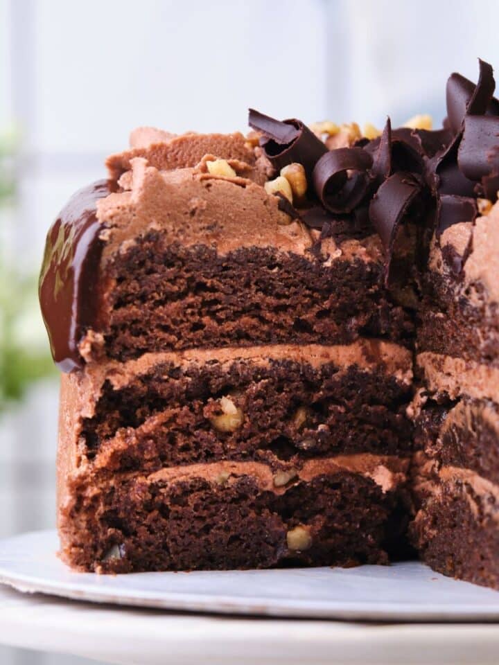 A three layer chocolate walnut cake cut open to show the moist layers.