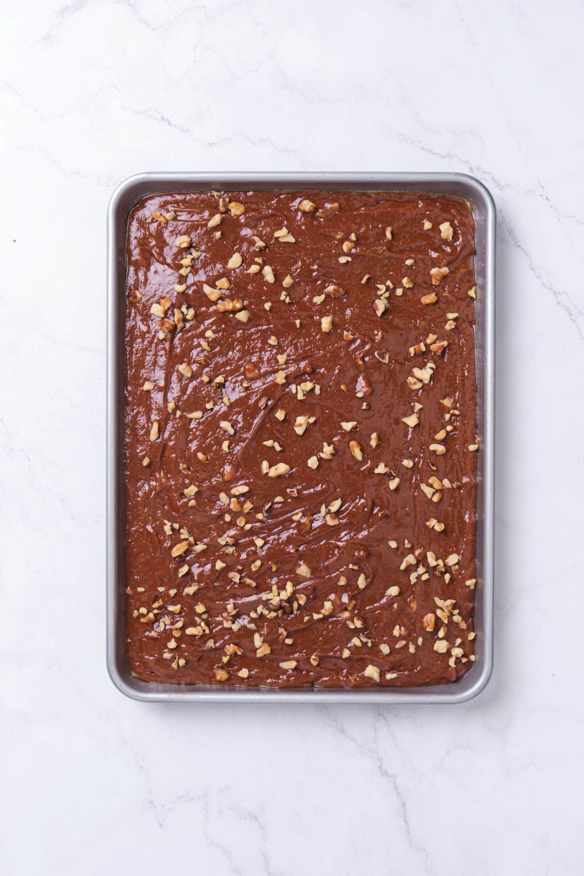 Chocolate cake batter in a sheet pan with nuts sprinkled on top.