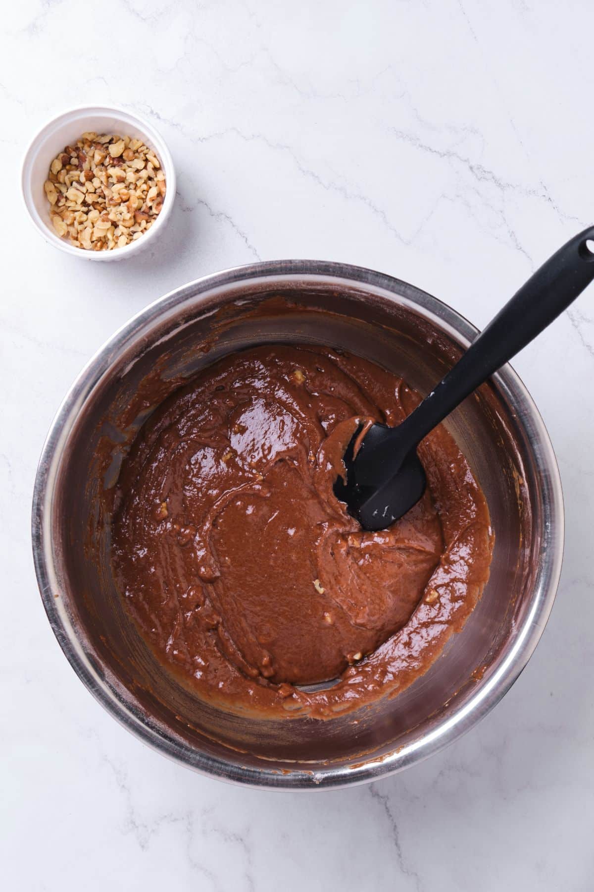 Chocolate cake batter in a bowl with chopped walnuts mixed in.