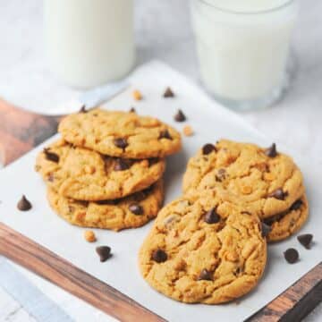 Several butterscotch chocolate chip cookies with 2 glasses of milk.