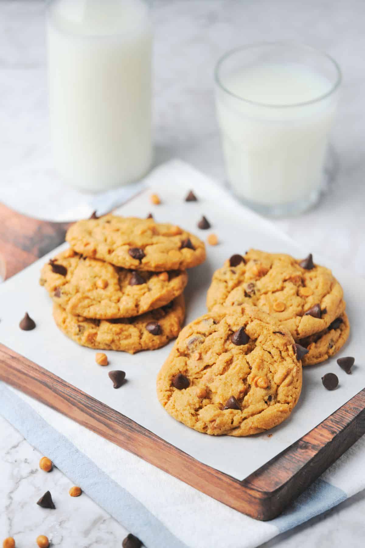 Several butterscotch chocolate chip cookies with 2 glasses of milk.