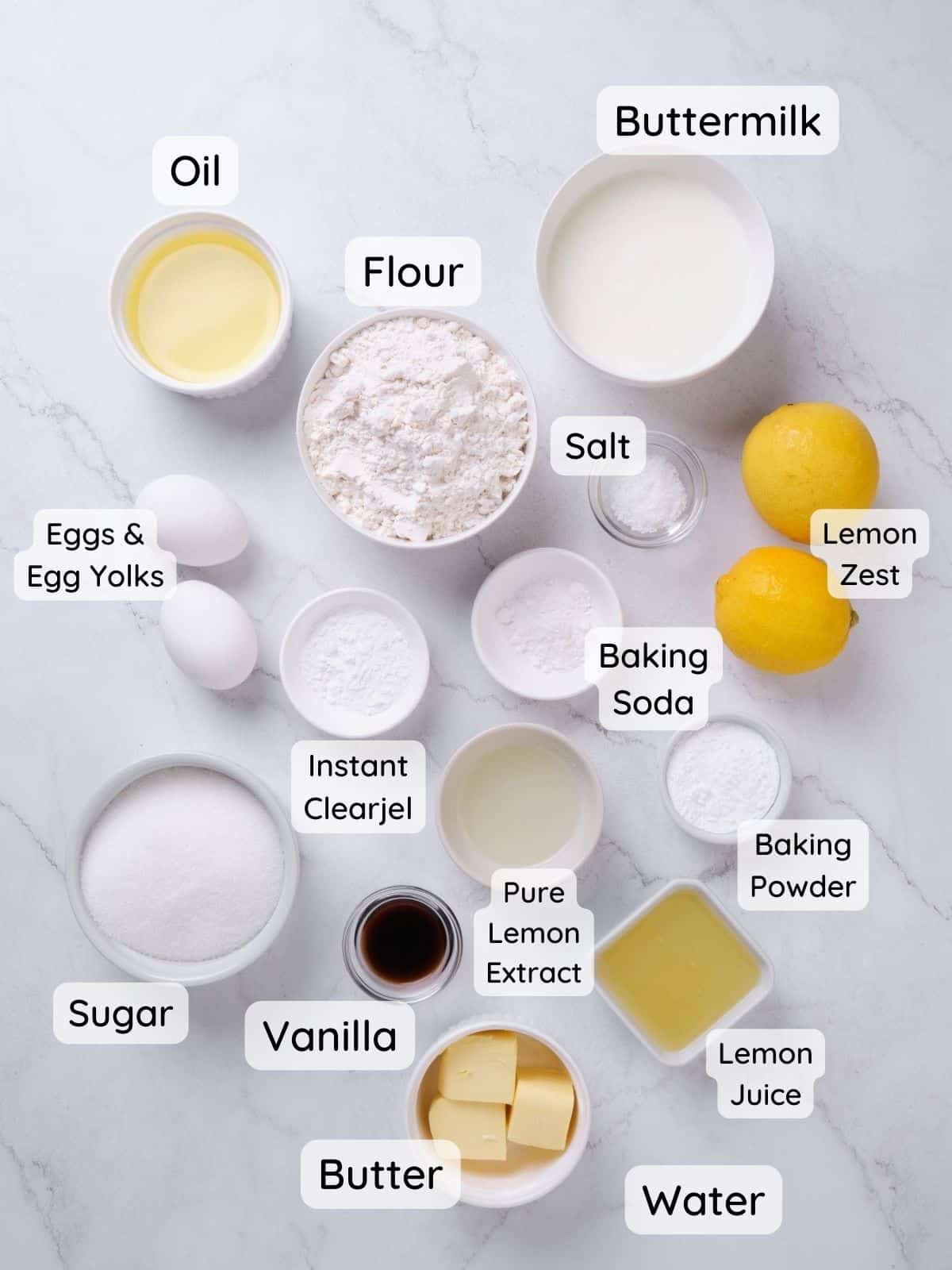 An overhead shot of the cake and lemon filling ingredients.  With the text "flour, sugar, baking powder, baking soda, salt, instant clearjel, butter, lemon zest, lemon juice, egg and egg yolks, vanilla, pure lemon extract, buttermilk."